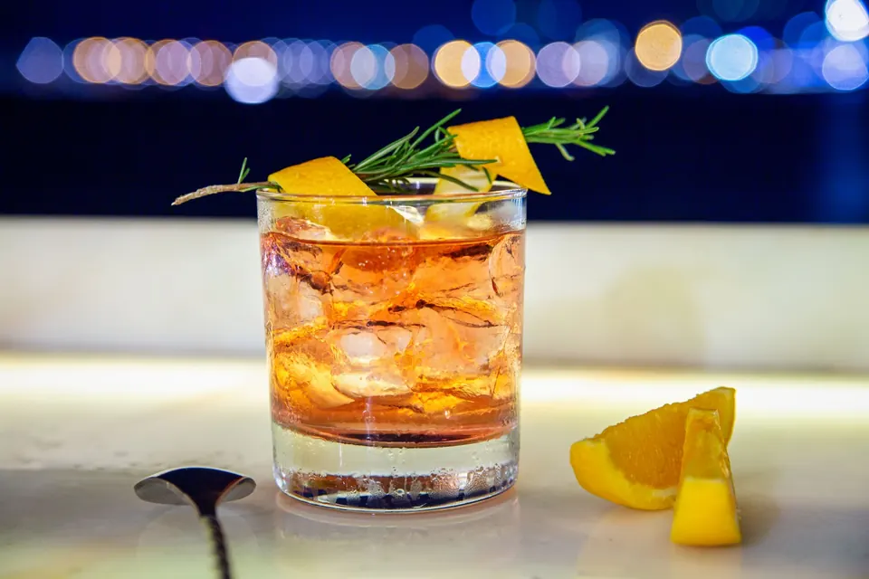 Citrus and rosemary old fashioned with city bokeh behind