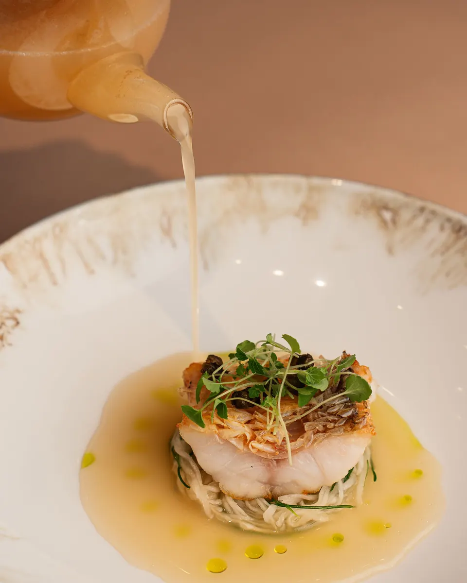 Golden broth poured around a delicate fish course with microgreens