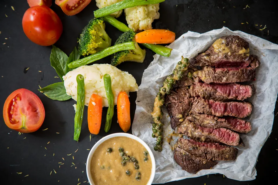 Sliced medium-rare steak beside roasted vegetables and sauce