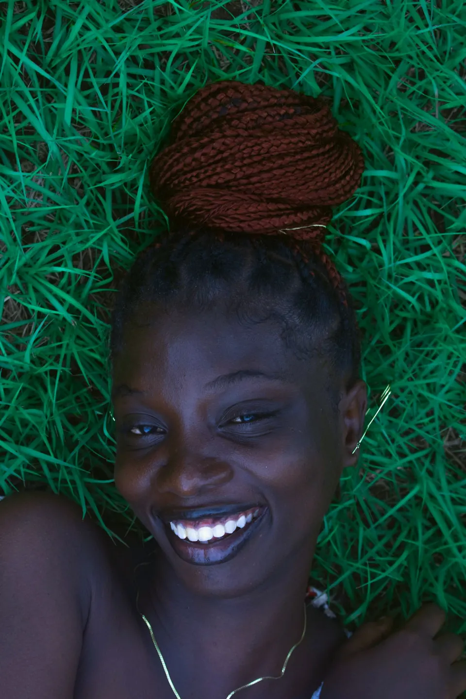Woman with braided hair laughing while lying in green grass