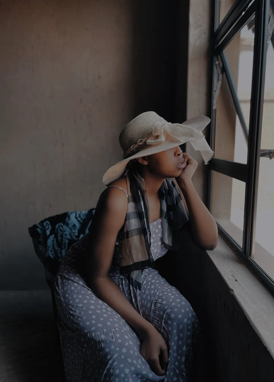 Woman in a sun hat sitting by a window, chin resting on her hand