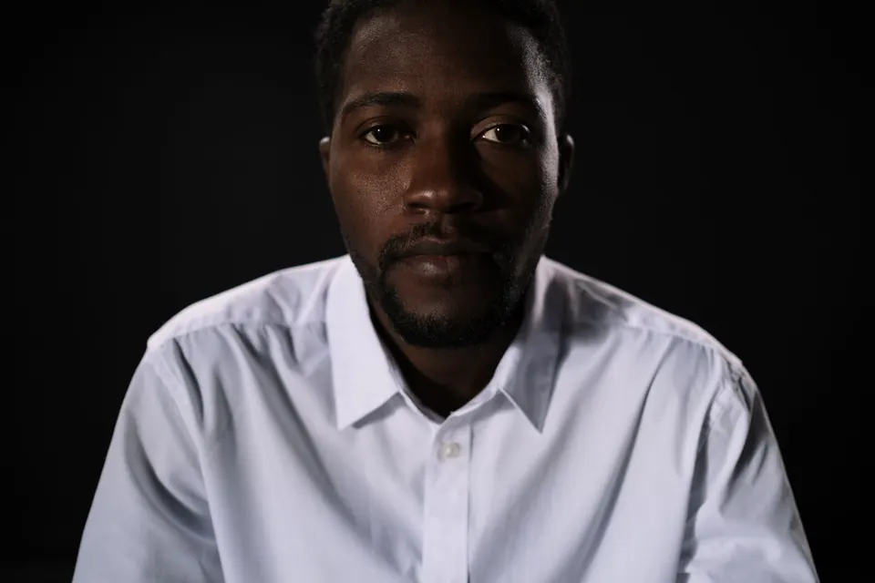 Man in a white shirt against a dark background, steady gaze